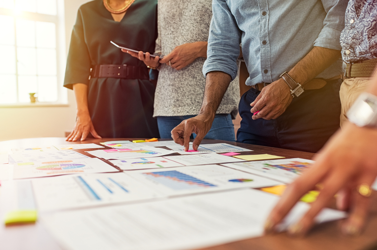 Businessmen and businesswomen discussing graphs showing results of successful teamwork. Group of business people having meeting together in conference room. Closeup of multiethnic business hands analyzing charts.